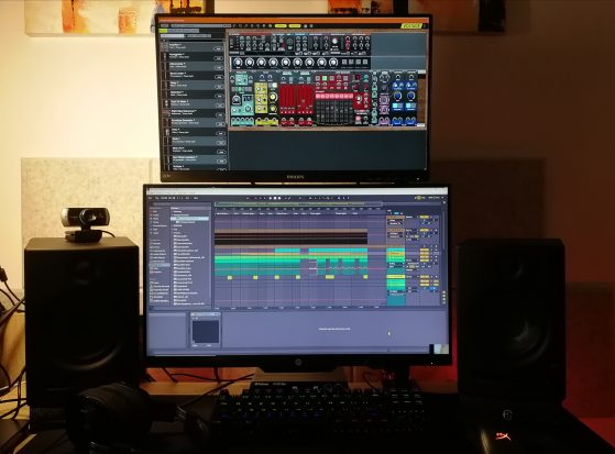 foto de setup para producción musical, con 2 pantallas de ordenador y dos monitores de estudio negros, con un teclado de pc de leds de colores.